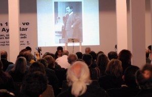 Keskin and Zarakolu address the audience. A photograph of Taniel Varoujan is seen in the background.