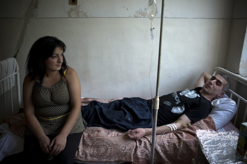 A young man in a hospital bed with his wife. He has a stomach ulcer and believes it is from working at the mine. (Photo by Nazik Armenakyan)