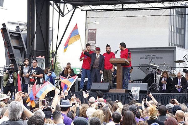 AYF Central Executive Member Gev Iskajyan delivers a message to Friday's crowd of marchers with Genocide survivor Paylag Titoyan accompanying him on stage. (Photo:Talin Mardirosian) 