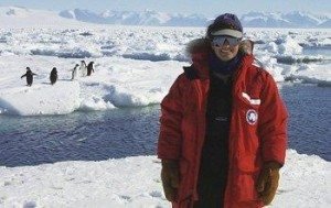 Dr. Deneb Karentz is bundled up in Antarctica with penguins frolicking behind her at a lake named after her.
