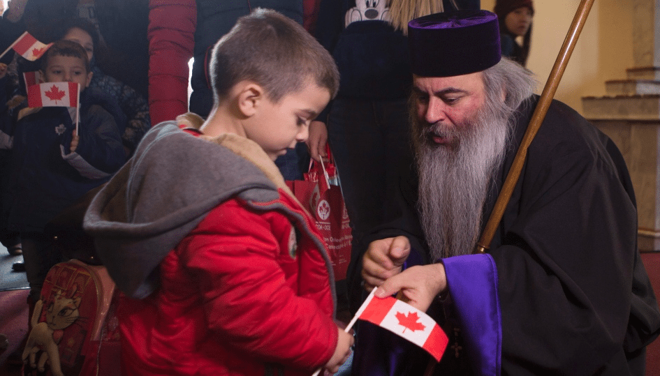 Bishop Meghrig Parikian, Prelate of the Armenian Apostolic Church of Canada, greets a Syrian newcomer. (Photo: CTV)