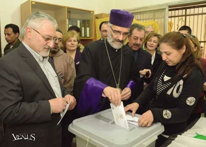 Prelate of Aleppo Archbishop Shahan Sarkisian (center) casts his ballot with Jirair Reisian (left) at a polling station in Aleppo (Photo: Venus Photography)